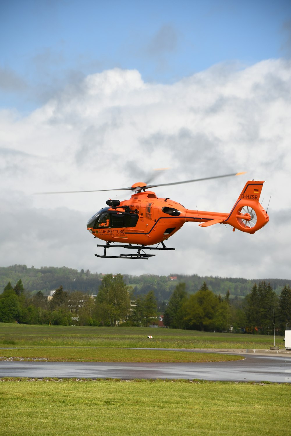 日中に緑の木々の上を飛ぶオレンジ色のヘリコプター