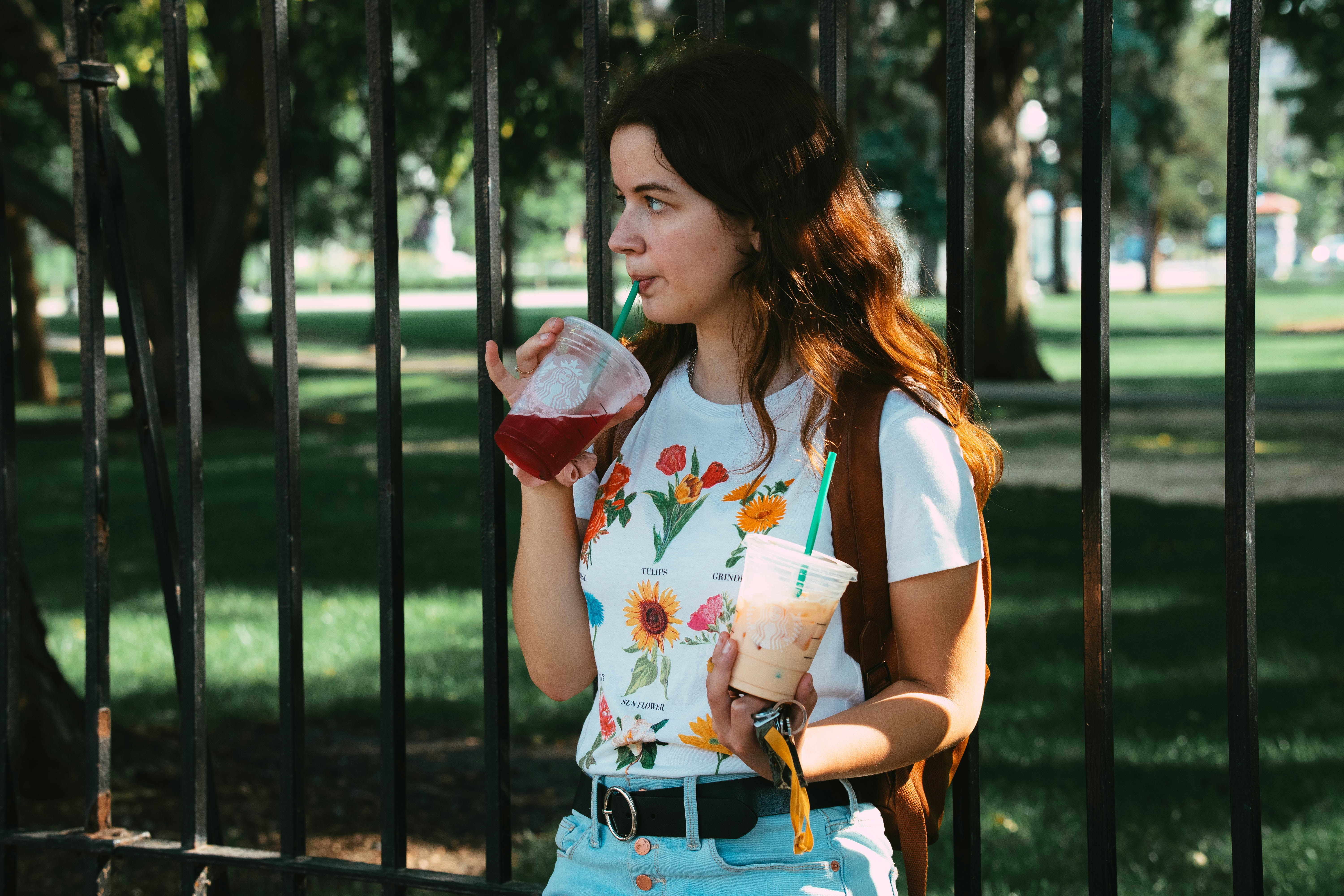 a woman standing in front of a fence drinking from a cup