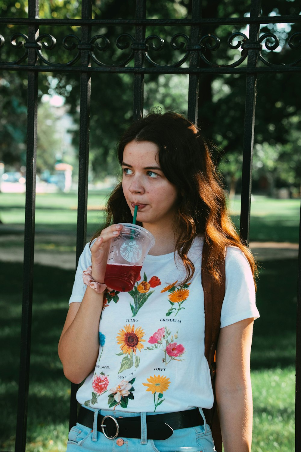 a young woman drinking a drink in front of a gate