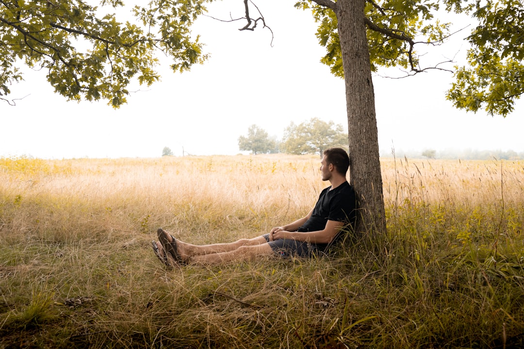 man in black t-shirt sitting on brown grass field during daytime