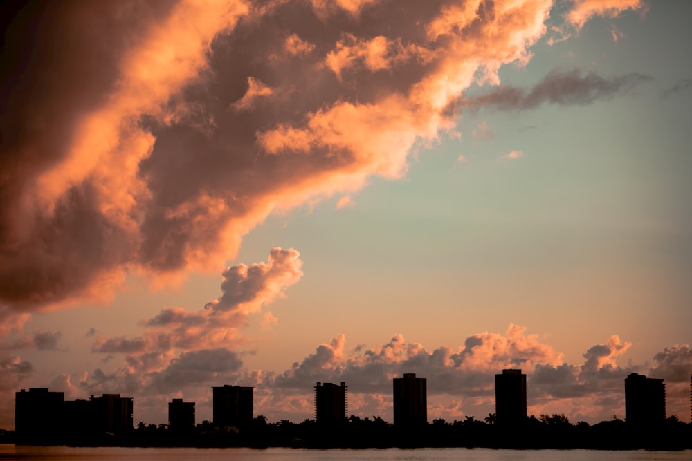 silhouette of city buildings under orange and gray cloudy sky during sunset