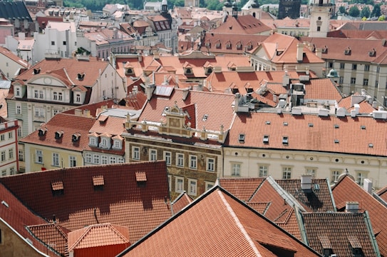The image captures a picturesque view of a European cityscape featuring a dense collection of historic buildings with distinctive red-tiled roofs. The architecture showcases classic design elements, such as gabled windows and ornate facades, indicative of an old-world charm. The photo provides a sense of the intricate urban layout with tightly packed rooftops and picturesque details.