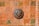 A ceramic artwork depicting a lion's head is mounted on a richly patterned terracotta tile wall. The tiles feature intricate green and orange motifs, adding to the rustic and artistic feel of the piece.