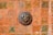 A ceramic artwork depicting a lion's head is mounted on a richly patterned terracotta tile wall. The tiles feature intricate green and orange motifs, adding to the rustic and artistic feel of the piece.