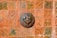 A ceramic artwork depicting a lion's head is mounted on a richly patterned terracotta tile wall. The tiles feature intricate green and orange motifs, adding to the rustic and artistic feel of the piece.