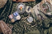 A collection of military items placed on camouflage fabric includes medals, patches, bullets, a tactical cap with a 'Don't Tread on Me' patch, and a brown holster.