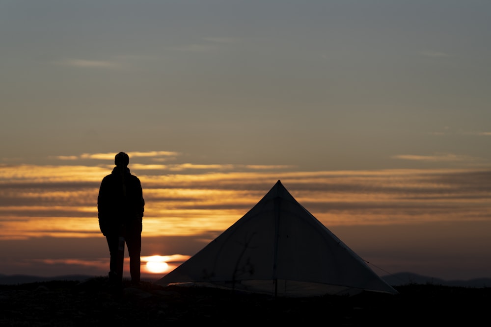 silhouette of man standing near tent during sunset