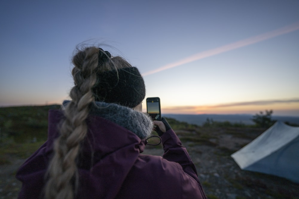 woman in purple hoodie taking photo of sunset