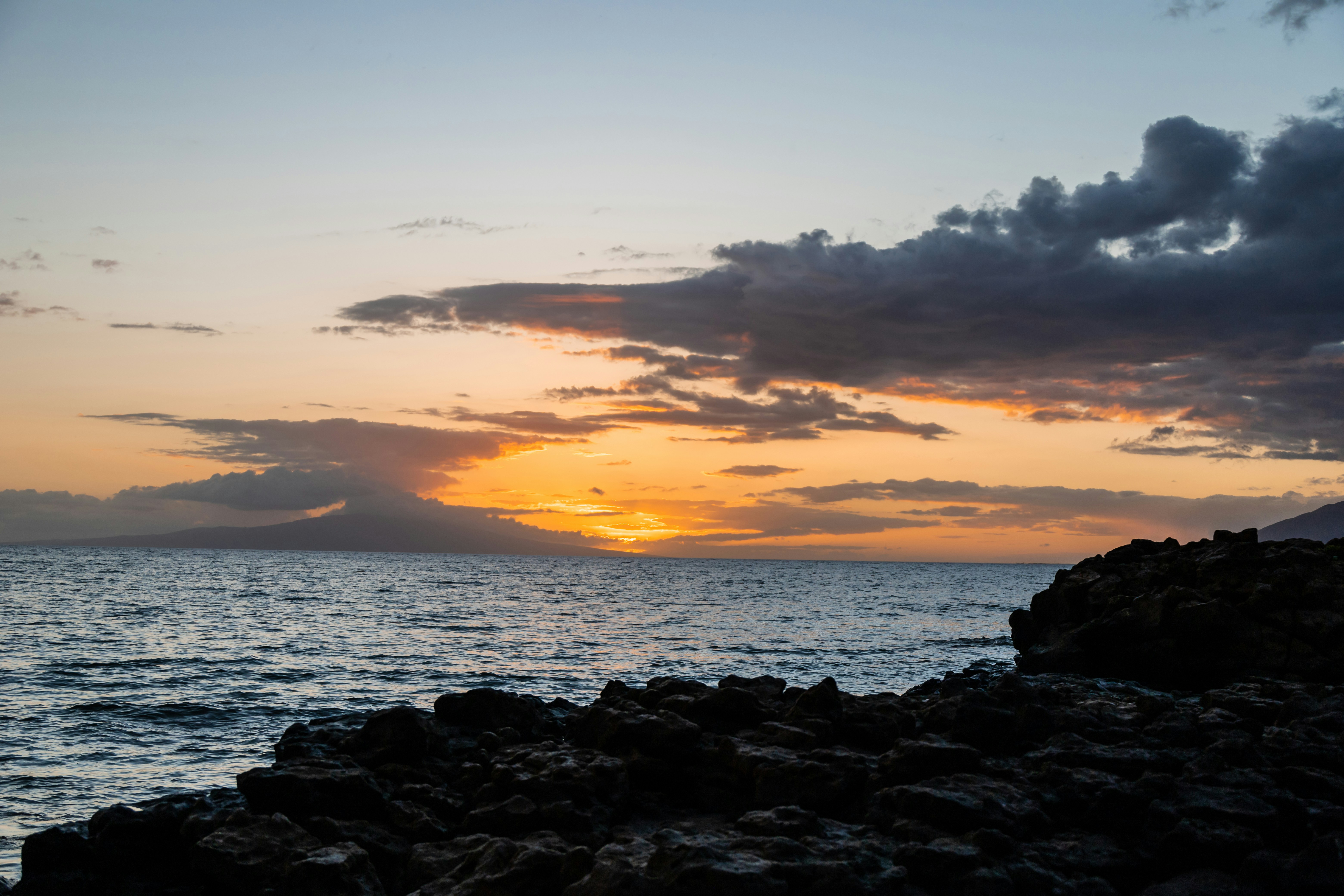 Black rocks on sea shore during sunset