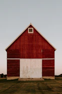 A freshly completed red post frame barn standing tall against a clear blue sky.
