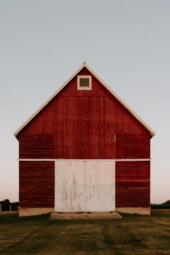 A freshly completed red post frame barn standing tall against a clear blue sky.