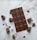A chocolate bar with a grid pattern is centered on a white marble surface, surrounded by chocolate chunks and crumbs scattered around.