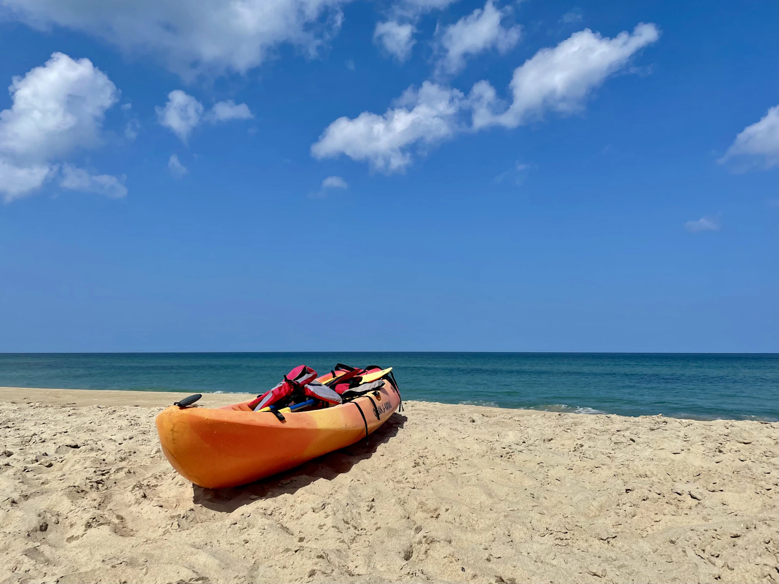 Real orange kayak resting on a sandy beach beside the ocean