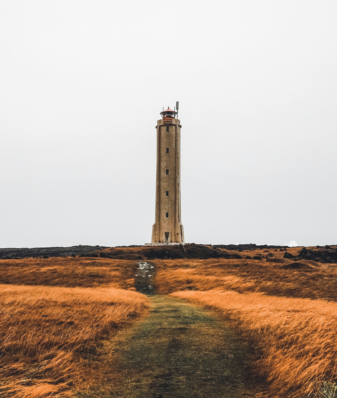 white lighthouse on brown grass field under gray sky