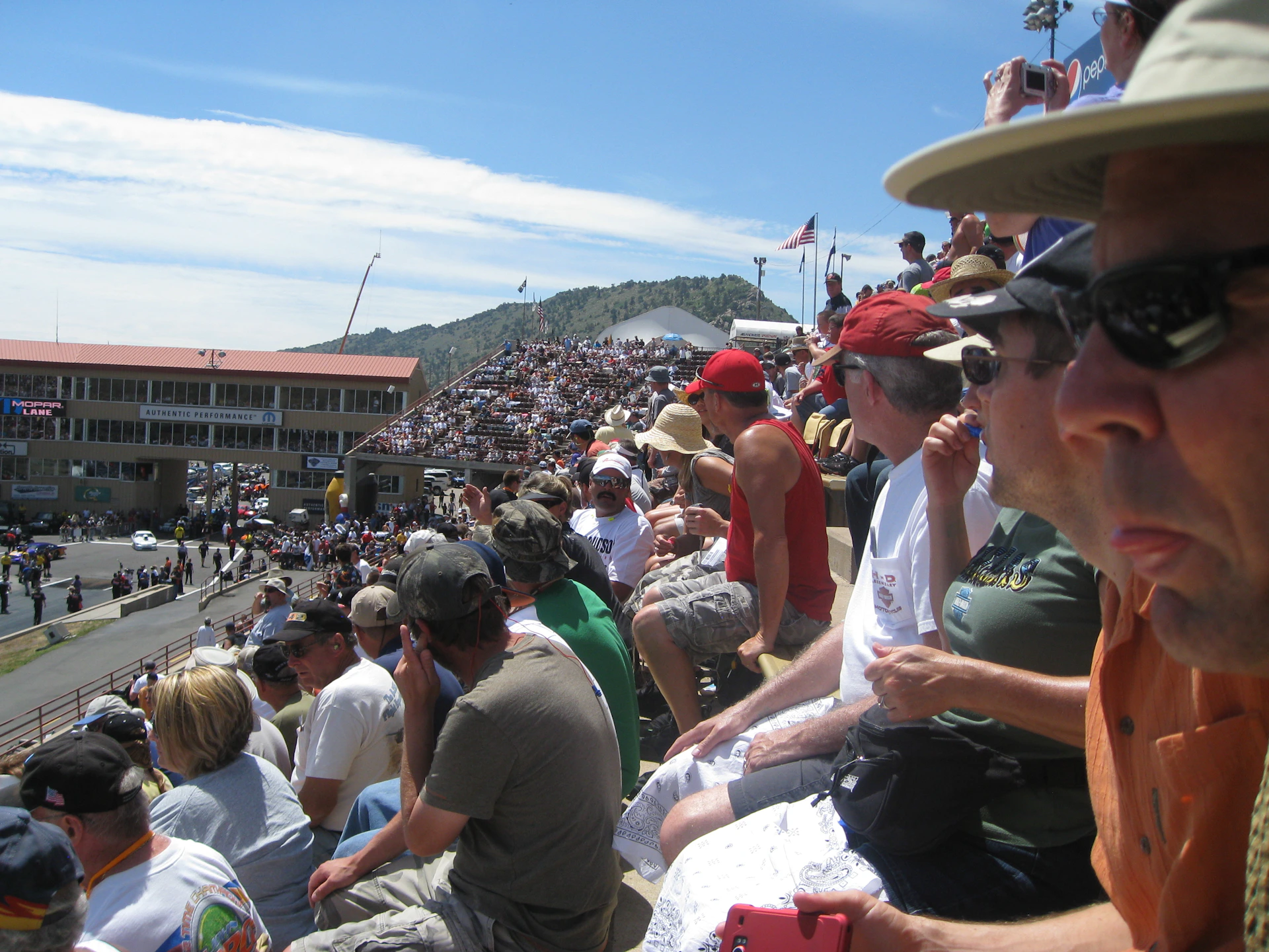 The grandstand filled with excited fans cheering, colorful banners waving, and the track bathed in golden afternoon light.