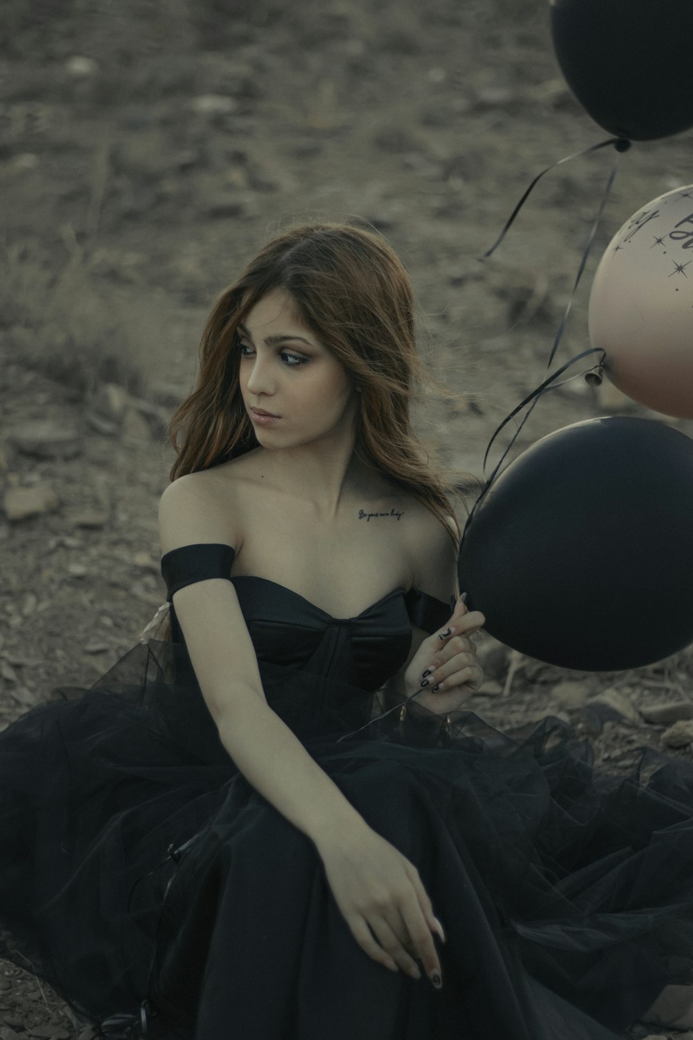 woman in black spaghetti strap dress lying on ground with black balloon