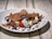 A delicious chocolate dessert crepe filled with whipped cream, bananas, and strawberries, topped with a scoop of chocolate ice cream and drizzled with chocolate syrup. Blueberries and crumbled brownie pieces add texture and sweetness.