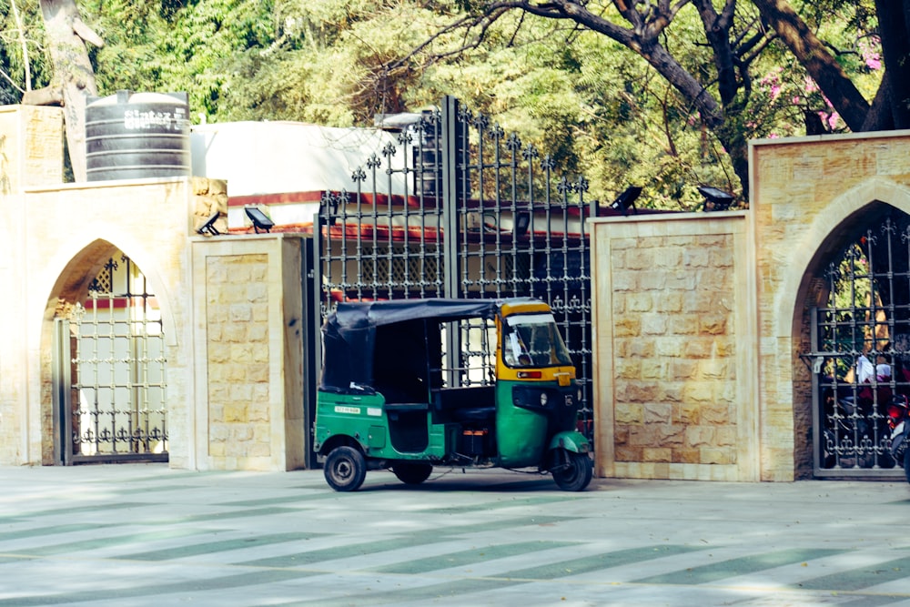 green and black auto rickshaw parked beside brown concrete building during daytime