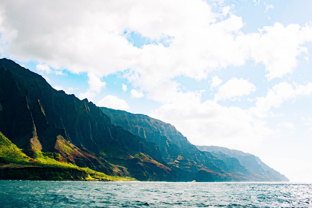 green and black mountain beside body of water during daytime