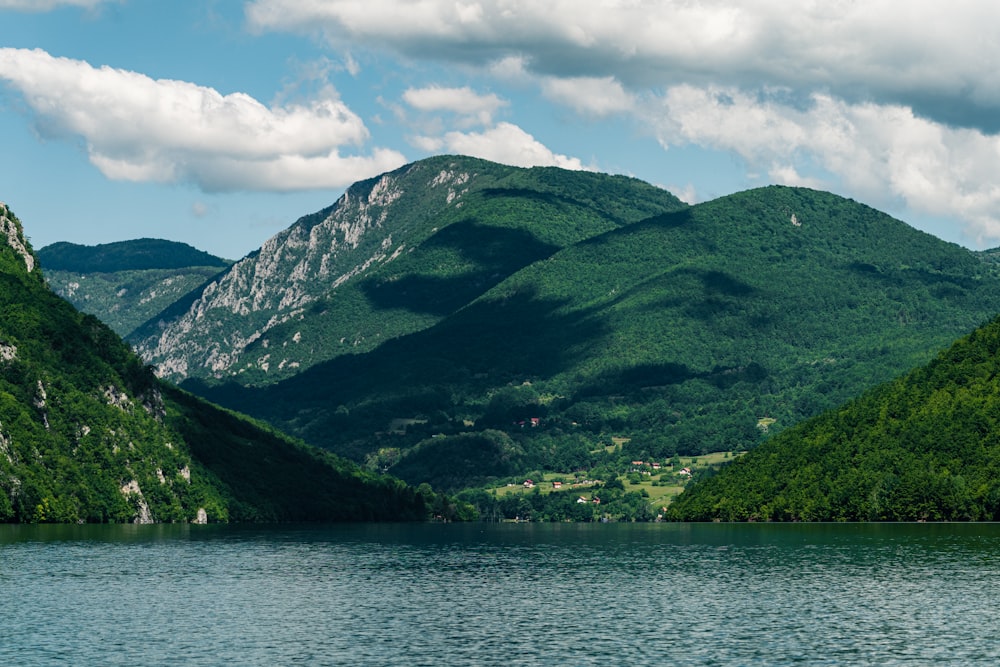 green mountains beside body of water under cloudy sky during daytime