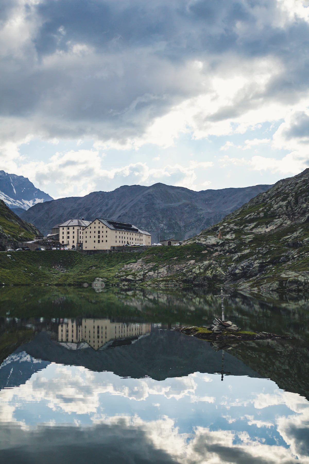 The Great St Bernard hospice reflected in the pass lake under heavy clouds
