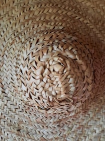 A close-up view of a woven straw hat with intricate patterns and a natural texture. The focus is on the center of the hat, highlighting the craftsmanship and details of the weave.