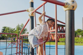 girl in white and gray floral dress standing on red metal bar