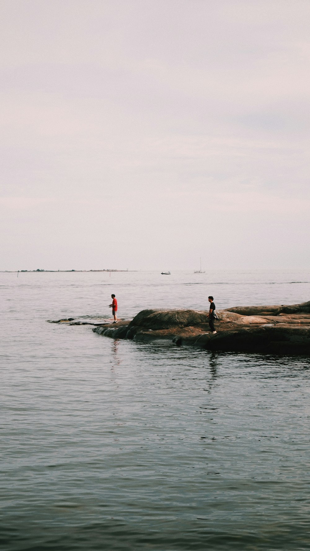 Persona con camisa roja de pie en la roca en medio del mar durante el día