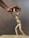 A wooden mannequin is positioned as if it's being supported or helped up by a larger human hand. The hand appears to gently hold the mannequin's upper body, illustrating an act of assistance or guidance. The background is neutral and plain, emphasizing the interaction between the hand and the mannequin.