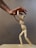A wooden mannequin is positioned as if it's being supported or helped up by a larger human hand. The hand appears to gently hold the mannequin's upper body, illustrating an act of assistance or guidance. The background is neutral and plain, emphasizing the interaction between the hand and the mannequin.