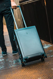 Stylish traveler walking through a sunlit city street carrying a Travora suitcase.