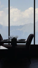 Elegant dining setup with mountain views through large windows at sunset.