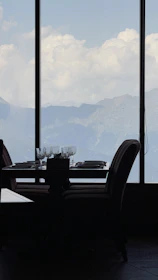 Elegant dining setup with mountain views through large windows at sunset.