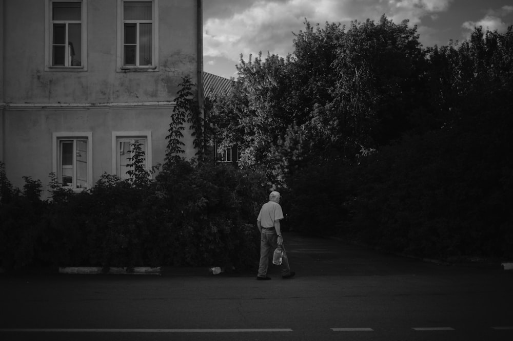 grayscale photo of man in white shirt and pants standing on road