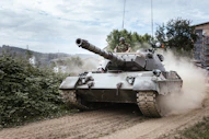 A military tank driving on a dirt road, kicking up dust, with a soldier visible