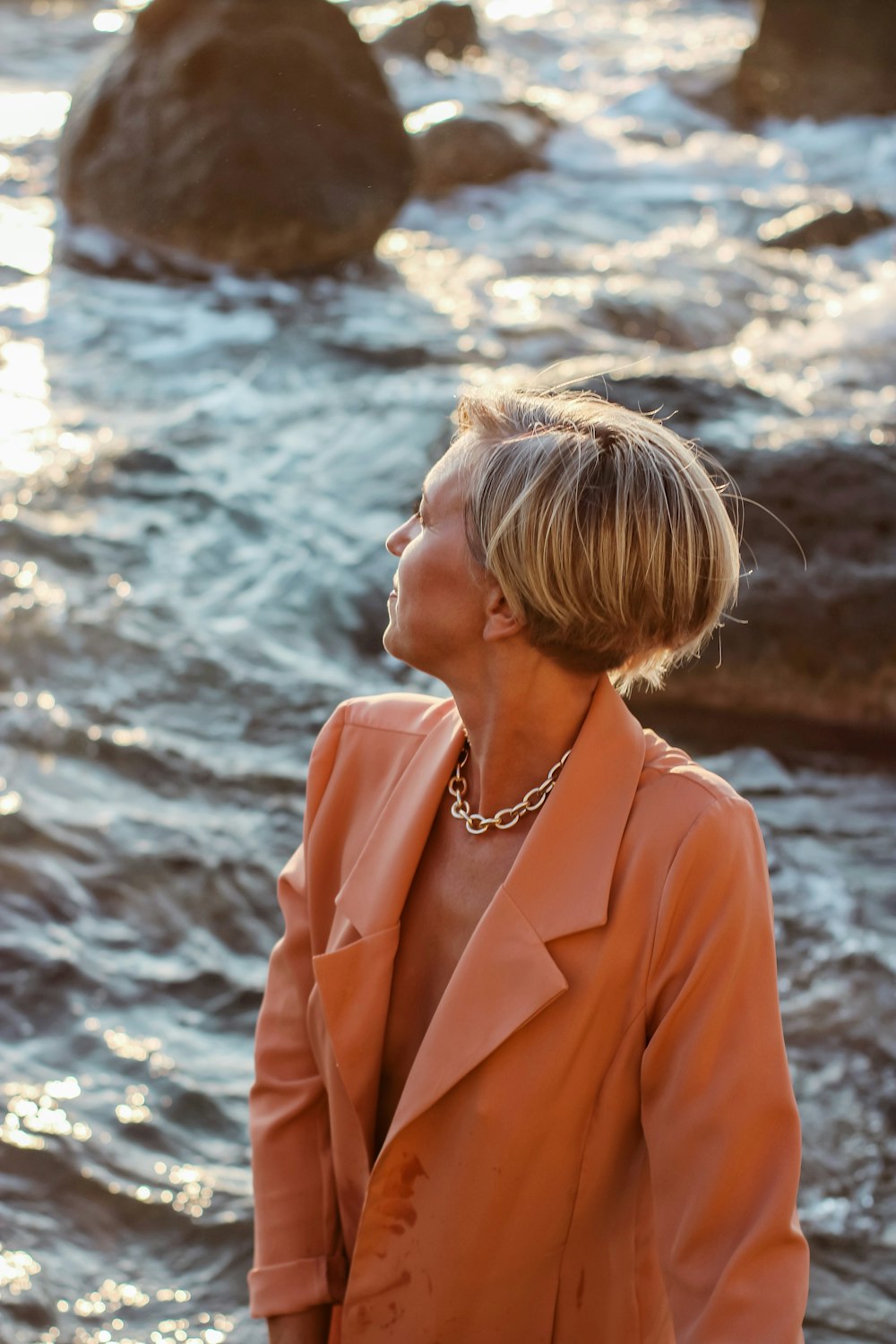 woman in orange blazer standing near body of water during daytime