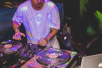 A DJ mixing on turntables with colorful lights in a small club setting.