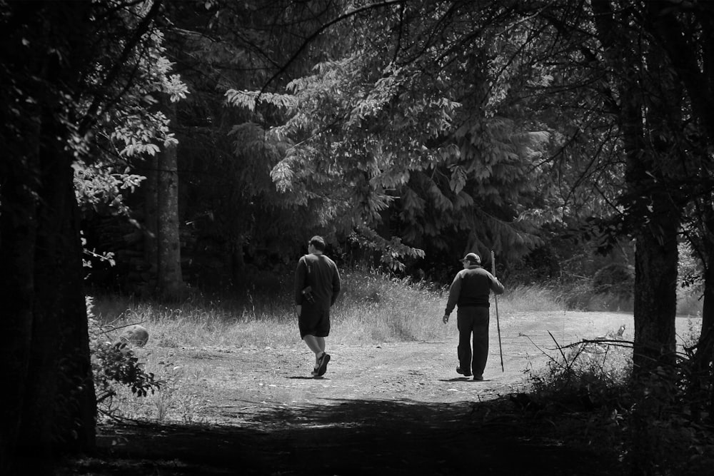 grayscale photo of 2 men walking on forest