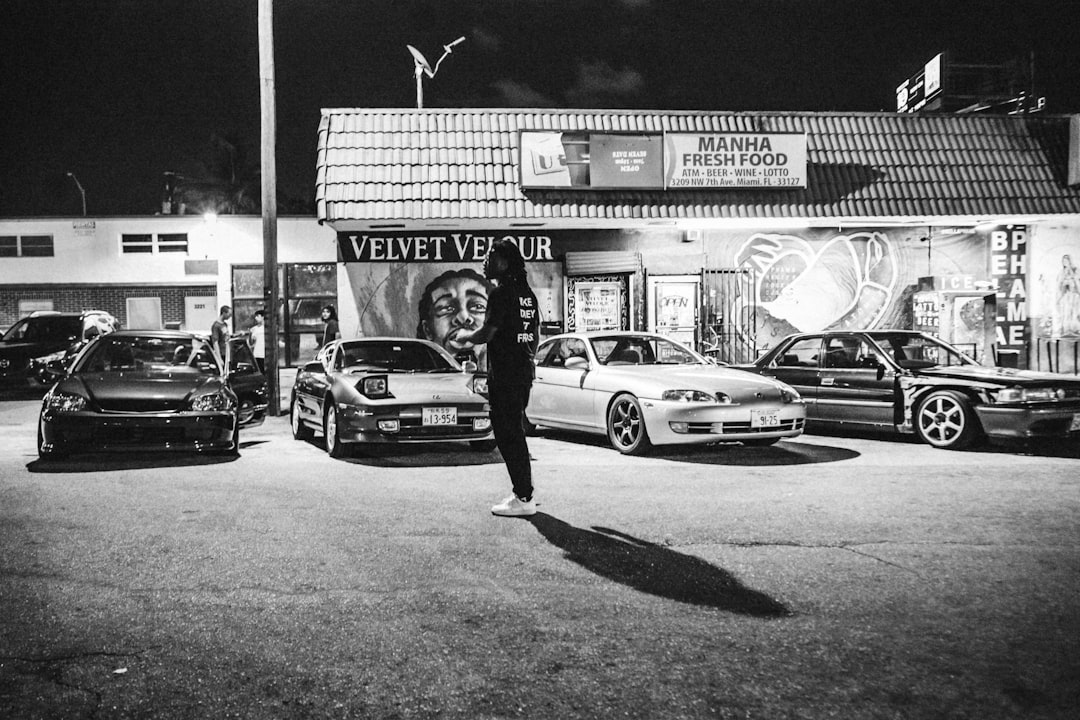 grayscale photo of woman in black jacket and pants standing beside car