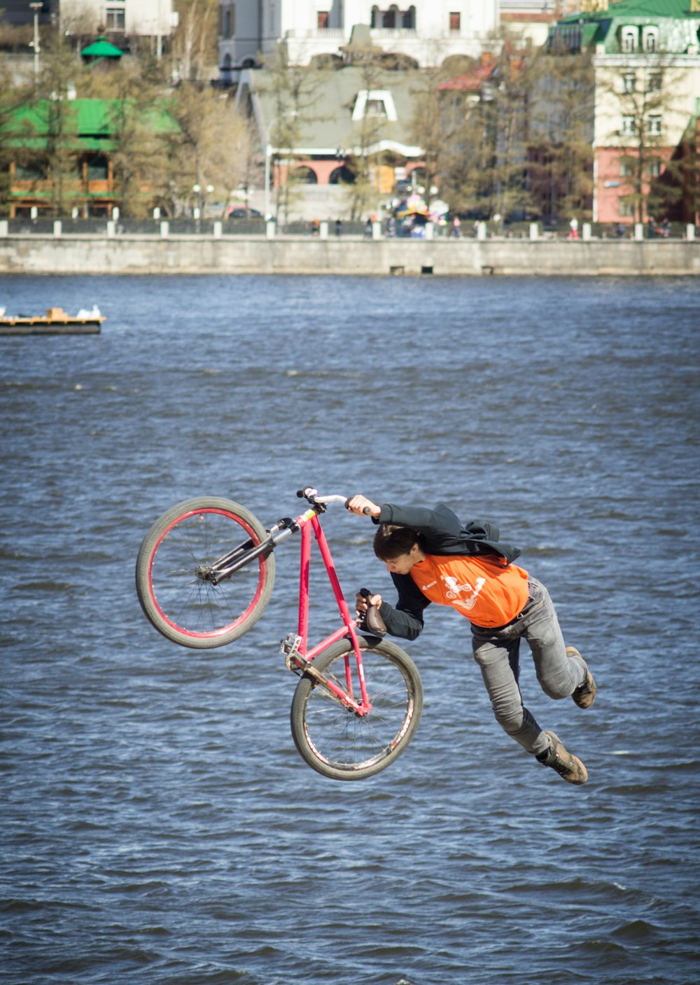 man in orange jacket and gray pants riding on red bicycle on body of water during