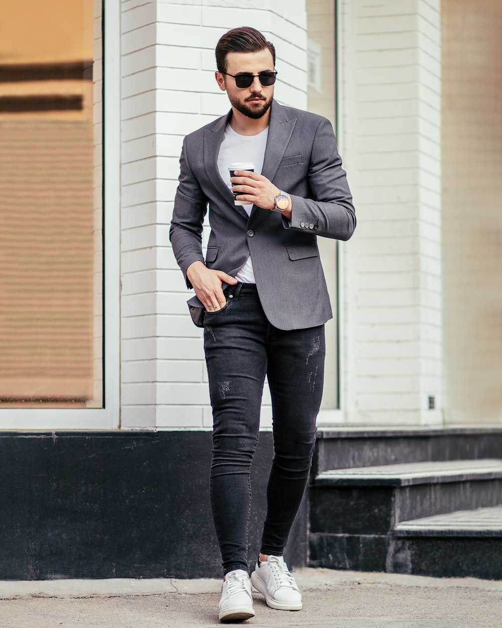 man in gray suit jacket and black pants standing beside white wall