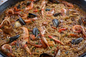 A close-up of a sizzling paella pan filled with vibrant seafood and fresh vegetables.