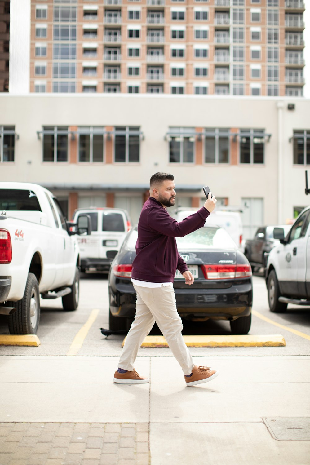 a man walking across a parking lot holding a cell phone