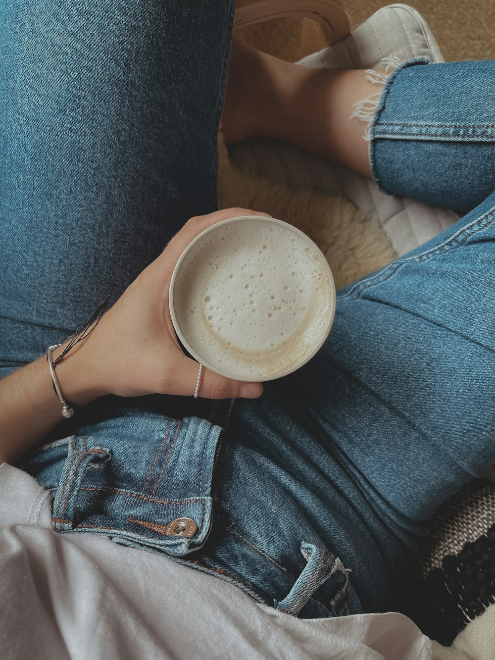 person in blue denim jeans holding white ceramic mug