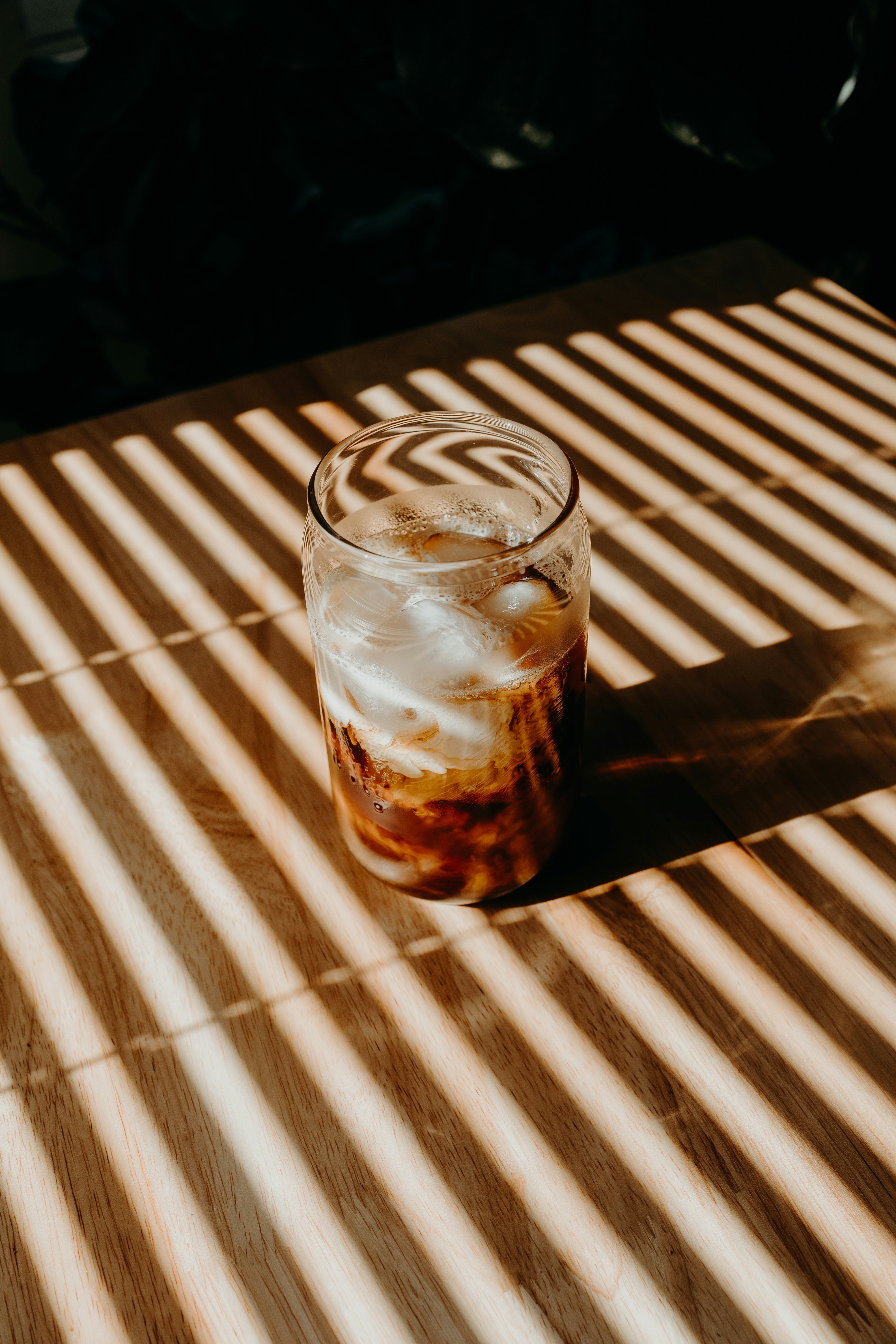Gelas minum bening dengan cairan coklat di atas meja kayu coklat
