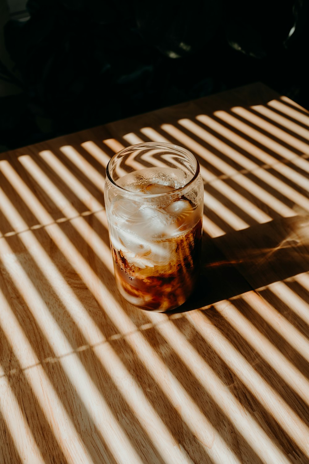 clear drinking glass with brown liquid on brown wooden table