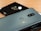 Two smartphones placed on a wooden surface, one is grey metallic with dual rear cameras and a brand logo, while the second is glossy black with a single camera and circular design around it.