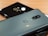 Two smartphones placed on a wooden surface, one is grey metallic with dual rear cameras and a brand logo, while the second is glossy black with a single camera and circular design around it.