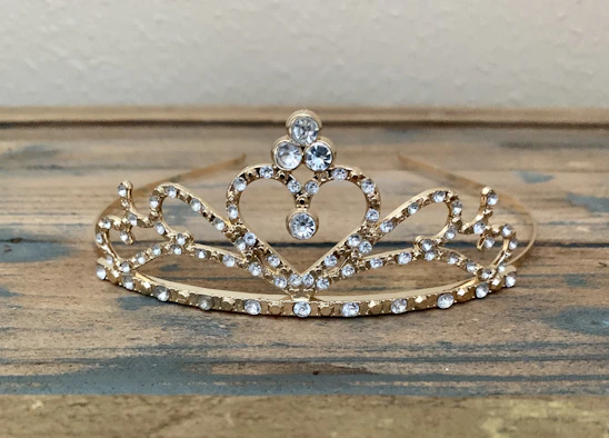Close-up of a delicate crystal bridal tiara resting on a soft velvet cushion, glowing gently in natural light.
