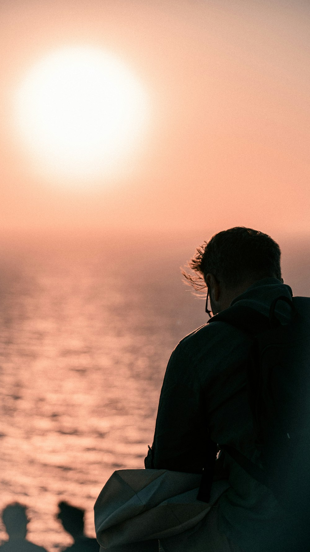 man in black jacket standing near sea during sunset